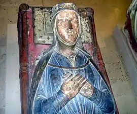 A photograph of a medieval tomb with a carving of Isabella on top. She is lying with her hands clasped, wearing a blue dress.