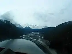 An aerial view down a river valley with glaciated mountains in the background.