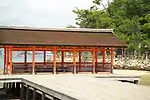 A half-open wooden building with a gabled roof on a platform over water.