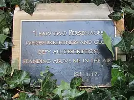 a black plaque surrounded by leaves with gold letters reading: "I saw two personages whose brightness and glory defy all description, standing above me in the air."