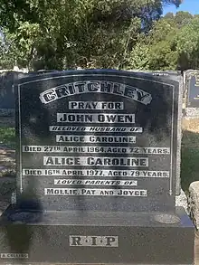 a colour photograph of a square-shaped gravestone of dark grey stone with pale lettering