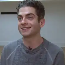 Ferver, a white person with close-cropped grayish hair sits in a white studio smiling