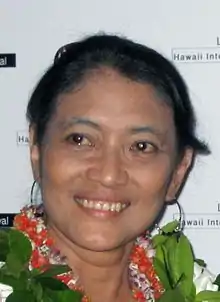 A colour photograph of a woman wearing a wreath of leaves looking left.