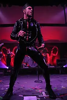 A Caucasian man wearing leather suit, performing on stage, facing right.