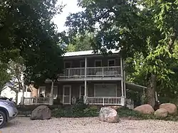 Photo of a red brick two-story home framed by trees, with the front of a gray car peeking into the left side of the photo.