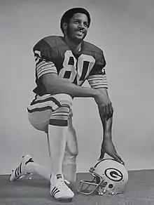 Lofton kneeling in uniform with his helmet off