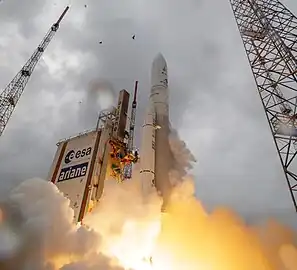 Low-angle shot of a light-colored rocket blasting up towards a gray sky