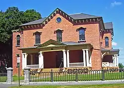 A brick house with pointed roof behind a metal fence