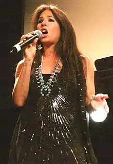 A woman holding a microphone and wearing a black dress with sequins and a necklace