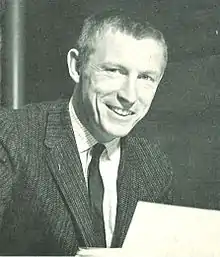 Jerry Burns wearing a suit and tie, holding a piece of paper