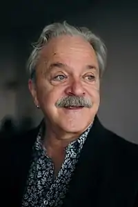 Headshot of a man with a mustache and an earring