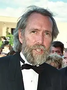 A tall, thin man in his early fifties, with salty-gray hair and a full beard, and wearing a tuxedo.