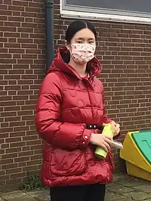 Photo of Zhu Jiner in 2022 wearing a patterned mask and a raincoat, holding a green item that could possibly be a water bottle.