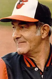 A man in a black jacket and black, white, and orange cap