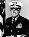 man in Navy uniform with cap, American flag in background