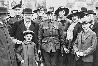 a black and white group photograph of a uniformed Leak with a group of admirers. Leak is holding the hand of a woman standing next to him.