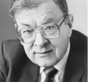 Black and white facial photo of an elderly man wearing eyeglasses and a suit and tie