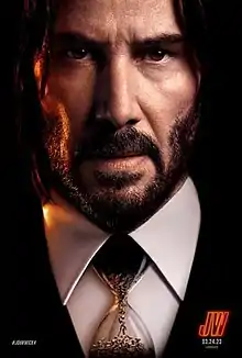 A closeup of John Wick, wearing an hourglass as a "tie", with bullets flowing into the lower bulb inside the hourglass.