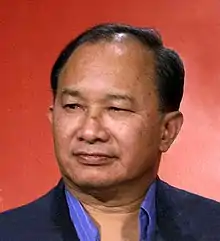 A photo of a Chinese man wearing a black suit against an orange backdrop.