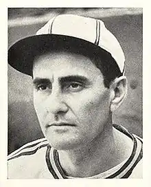 A man in a white baseball jersey and cap with dark stripes looksto the left.