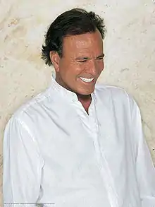 A man smiles and looks down. He is wearing a plain, white shirt.