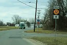 A two-lane road in a developed but semi-rural area. A sign advises trucks to continue straight for K-32 Truck.