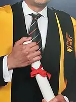 Individual holding a diploma, wearing an academic gown with a black epitoge over the left shoulder