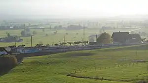 Train amid green fields with station building distance