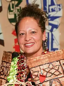 Head and shoulders of Karlo Mila smiling at the camera, she has her hair up and a cloak made from Tapa cloth