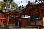 Building with white walls, red wooden beams and forked finials on the roof located behind a fence with gate.