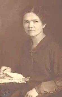 A woman in a sailor suit seated at a desk with her right hand on a manuscript