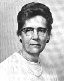 An older white woman wearing glasses, a crew-neck top, and a strand of pearls.