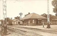 A sepia-tone postcard of a small railroad station and freight house