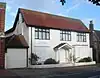 A converted house whose downstairs windows and entrance door are covered with white-painted panels. The three upper-storey windows are glazed and have brown frames.  An entrance porch is carried on spindly columns.