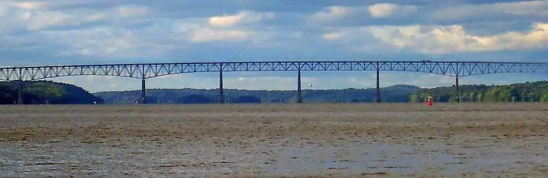 Panorama of a bridge over a wide river with mountains visible in the distance.