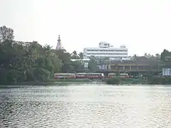 View across a lake of buses, trees and an urban skyline