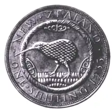 A plaster model of a design for the New Zealand shilling. An abstract kiwi, feathers textured in a rippled effect, is facing left. To the left, right, and above the bird are abstract wood-carving designs. Textured grass, consisting of many small ovals, is below the bird. Surrounding the kiwi is a rope-like circle, bordered by the text "NEW ZEALAND, ONE SHILLING, 1933"