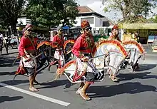 Men ride rattan horses while spectators watch