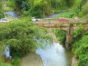 Photograph of a narrow, concrete bridge with traffic, over a small river