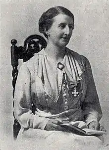 Black and white portrait of Laurie Annie Wilson taken in approximately 1925. She is seated, looking away from the camera, a book in her lap and what is presumed to be here MBE pinned to her dress.