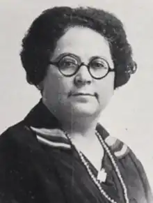 A middle-aged white woman with wavy dark hair, wearing eyeglasses