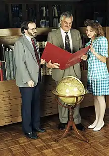 Two men and a young woman standing around a globe and looking at a red folder