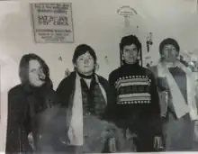 Four women, looking sombre, and a baby inside a gallery. On the walls behind, Anna Keir's drawings and Helen Wilson's poster, from the gallery's opening show in Harris Street, 1980.