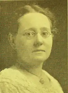 Portrait photograph of a middle-aged woman wearing a white blouse and glasses, her hair pulled back