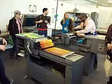 Kennedy operates a press while three people watch.