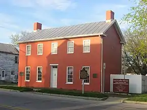 Small rectangular red brick house with white roof and many windows