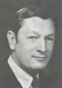 Headshot of a clean-shaven man in a suit, with short, slicked-back hair