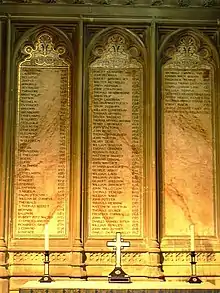 Three plaques on a wall, inscribed with the lists of the archbishops. In front of the plaques is a table with two candlesticks flanking an upright cross.