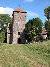 A red sandstone church with a pyramid tiled roof to the tower