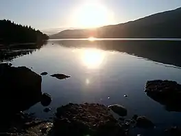 A lake at sunrise, flanked by trees and hills